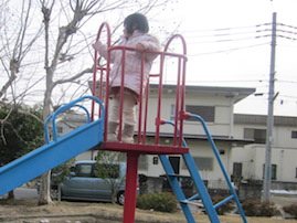 写真画像：公園のすべり台から公園を眺める子ども